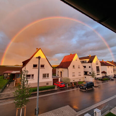 001_003 Ein Regenbogen ist über einer Reihe von Häusern zu sehen, während die Sonne die Szene in goldenes Licht taucht.