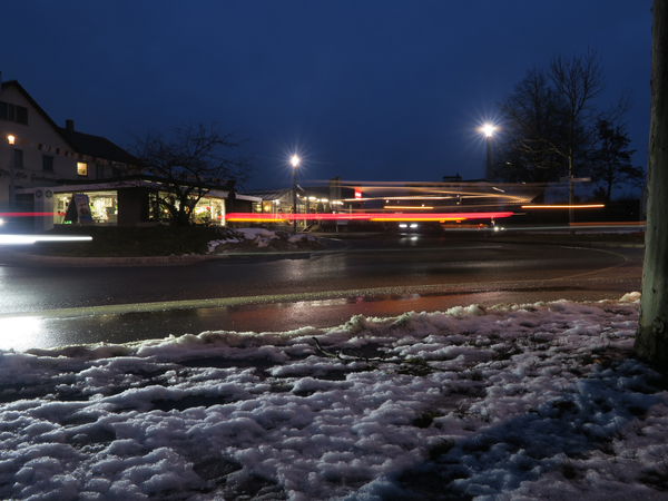 004_004 Eine nächtliche Straßenszene mit verschwommenen Lichtern von vorbeifahrenden Autos und Schnee am Straßenrand.