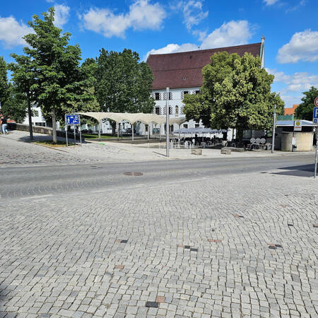 014_001 Das Bild zeigt eine große gepflasterte Fläche und im Hintergrund hinter Bäumen das Rathaus