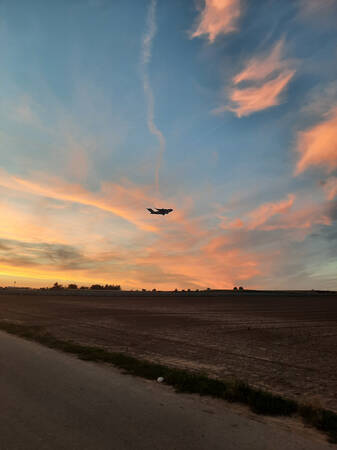 017_001 Das Bild zeigt die schwarze Silhouette eines Flugzeugs über einem großen Feld bei Sonnenuntergang
