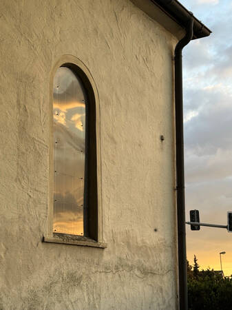 019_003 In dem Fenster einer Kapelle spiegelt sich der Abendhimmel