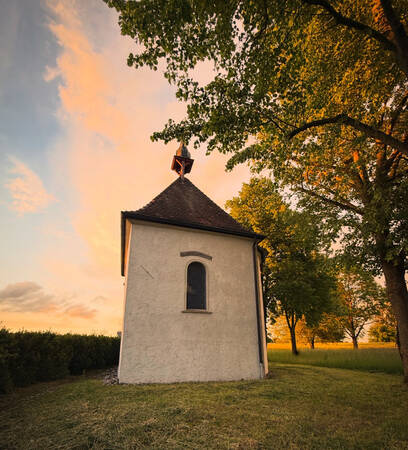 019_004 Eine kleine Kapelle steht auf einem von Bäumen umsäumten Platz, im Hintergrund wunderschöner warmer Abendhimmel