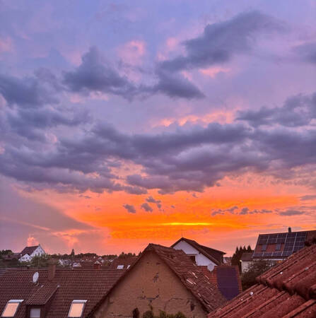 020_001 Ein farbenprächtiger Sonnenuntergang mit orange- und violett-gefärbtem Himmel erstreckt sich über den Dächern einer Stadt mit einer Kirche im Hintergrund.