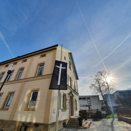 021_002 Vor einem historischen Gebäude hängt eine Fahne mit einem weißen Kreuz auf schwarzem Grund