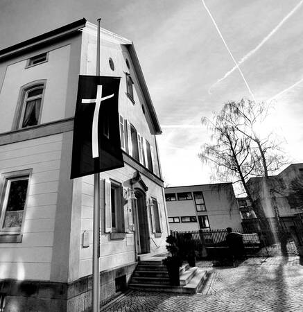 021_003 Schwarzweiß-Aufnahme: Vor einem historischen Gebäude hängt eine Fahne mit einem weißen Kreuz auf schwarzem Grund