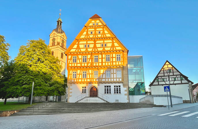 023_002 Dieses Bild zeigt ein historisches Fachwerkhaus und im Hintergrund eine Kirche in einer außergewöhnlich hellen Abendsonne