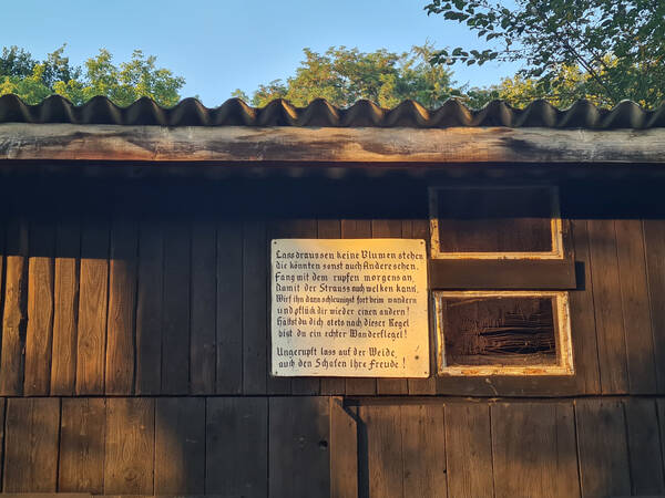 030_002 An einer Scheunenwand hängt ein Schild mit einem Text über das Pflücken von Blumen