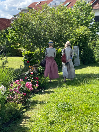 032_001 Zwei sommerlich gekleidete Damen mit Hut stehen bewundernd in einem gepflegten und schönen Gasten voller Blumen