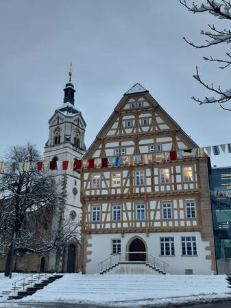 033_002 Das Bild zeigt ein historisches Fachwerkhaus und eine Kirche in schneebedeckter Landschaft mit Fasnetsfähnchen