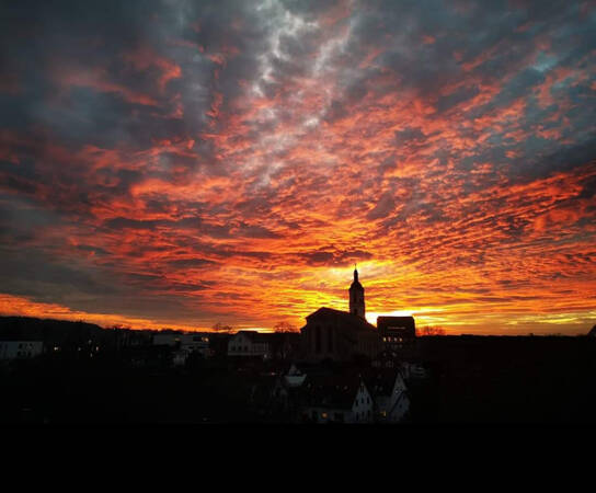 6. Platz M. u. H.-J. Fath: Ein beeindruckender Sonnenuntergang taucht den Himmel in leuchtende Orange- und Rottöne über einer Stadtsilhouette mit einem Kirchturm.