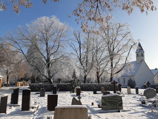 10. Platz Isabell Haas: Eine schneebedeckte, winterliche, sonnendurchflutete Friedhofslandschaft mit einer sehr schönen kleinen Kapelle im Hintergrund