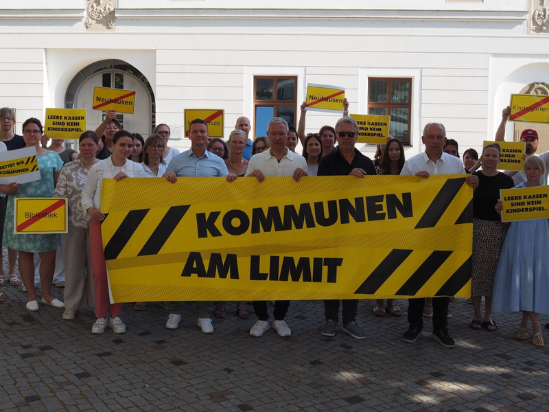 Eine Gruppe von Menschen steht vor einem Gebäude und hält Protestschilder mit der Aufschrift "KOMMUNEN AM LIMIT" hoch.